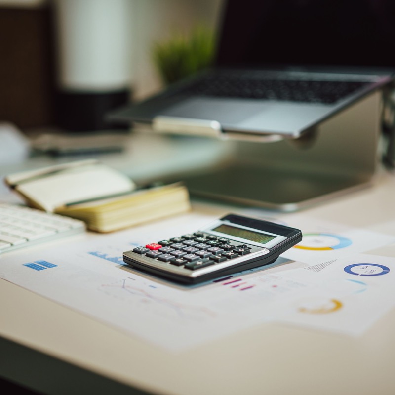 Calculator and documents on a desk beside an open laptop