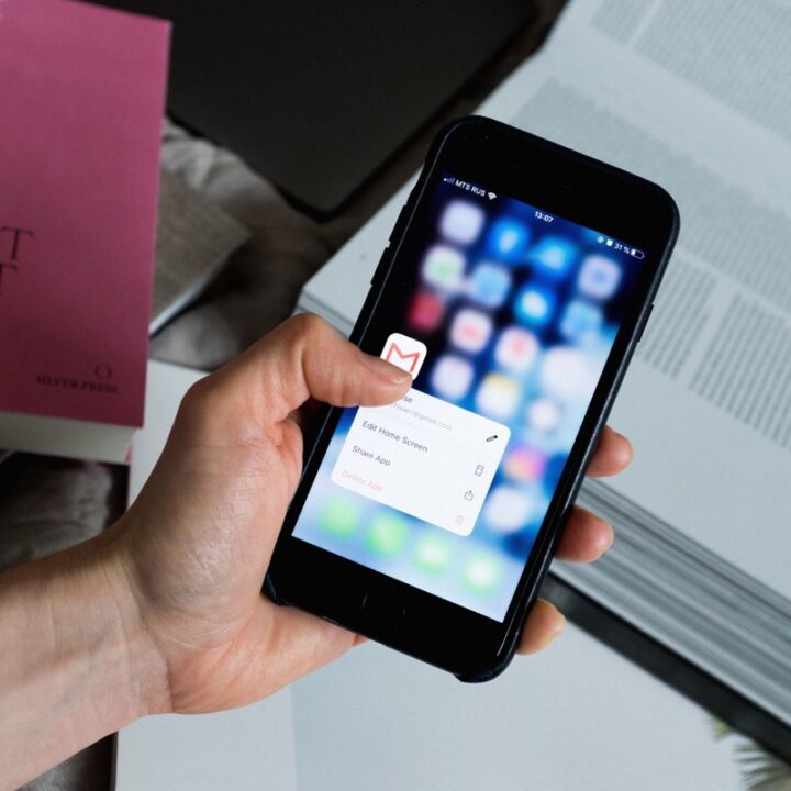 Hand holding a smartphone with an email app open beside a laptop and books